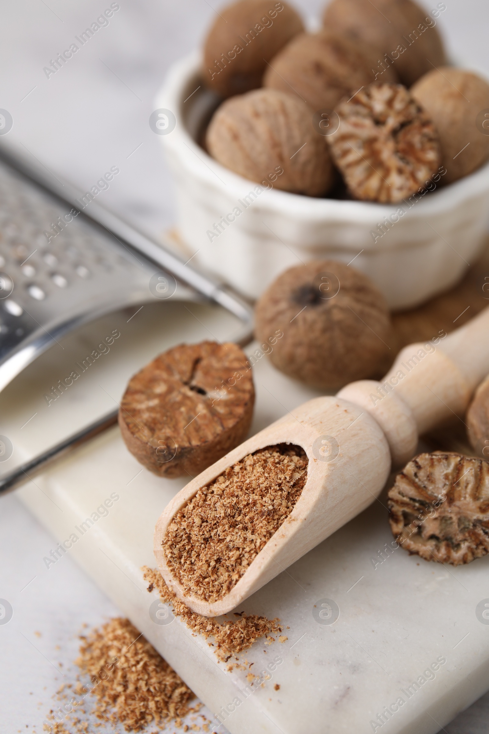 Photo of Scoop with grated nutmeg, seeds and grater on white table