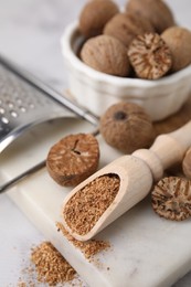 Scoop with grated nutmeg, seeds and grater on white table