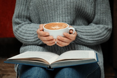 Woman with cup of coffee reading book at home, closeup