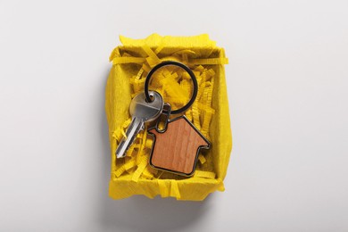 Photo of Key with trinket in shape of house and gift box on light grey background, top view. Housewarming party