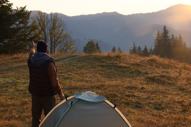 Tourist enjoying sunrise near camping tent in mountains, back view