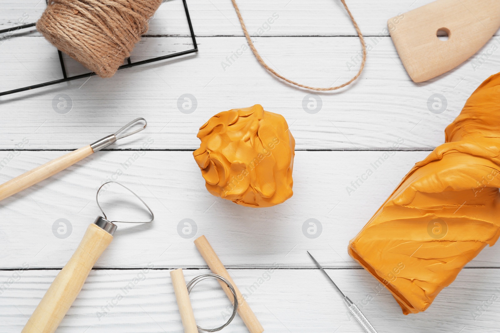 Photo of Clay and set of modeling tools on white wooden table, flat lay