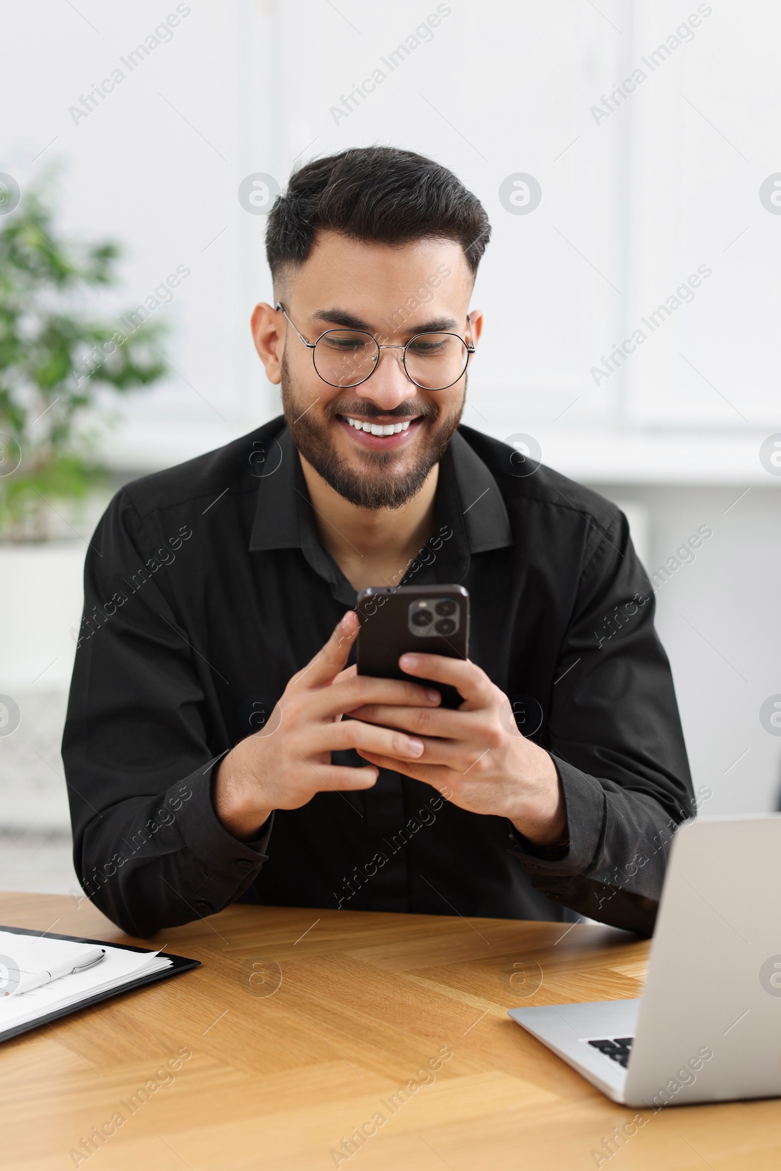 Photo of Handsome young man using smartphone at wooden table in office