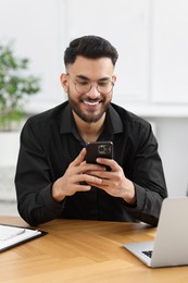 Photo of Handsome young man using smartphone at wooden table in office