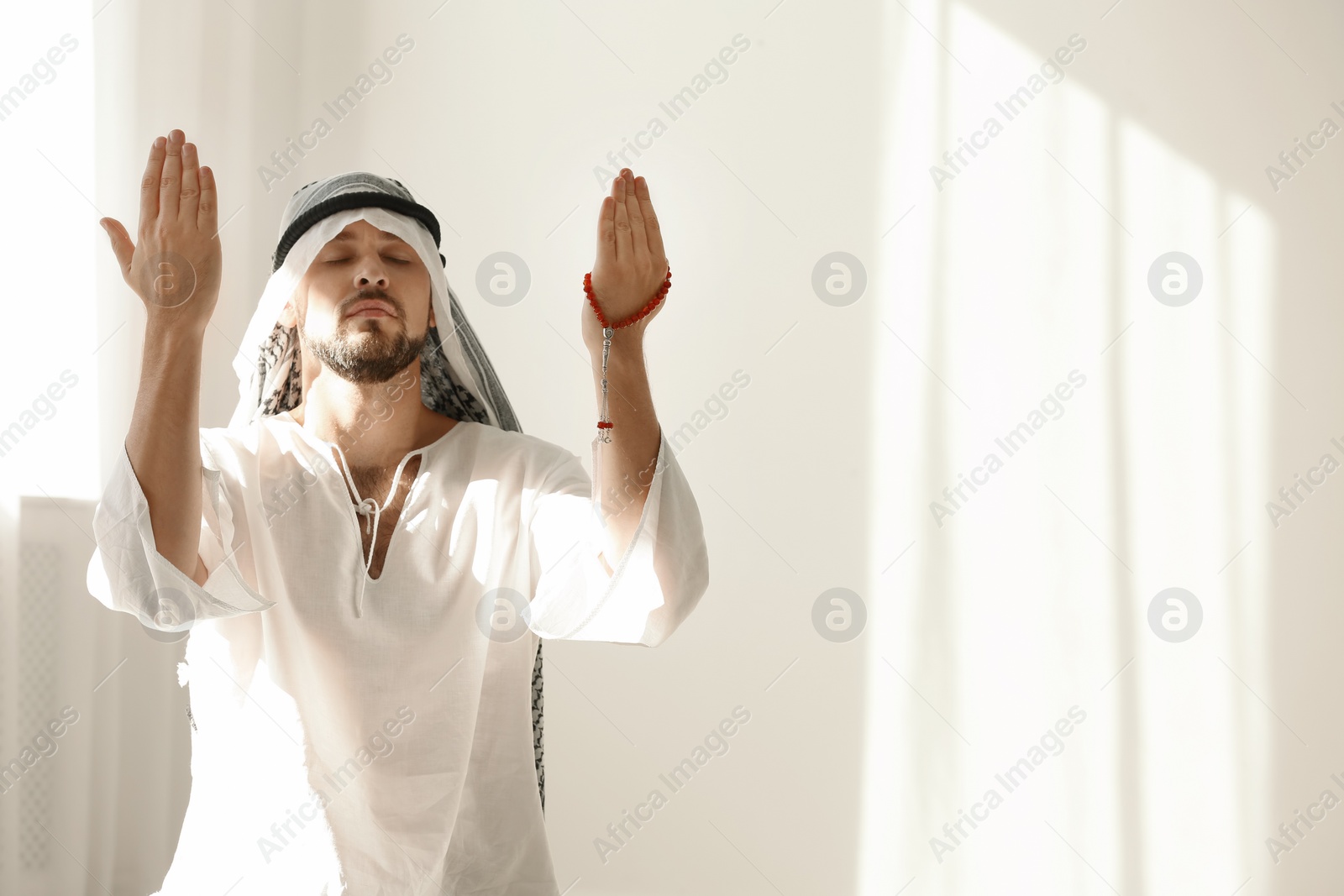 Photo of Muslim man in traditional clothes praying indoors. Space for text