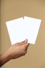 Photo of Man holding sheets of paper on beige background, closeup. Mockup for design