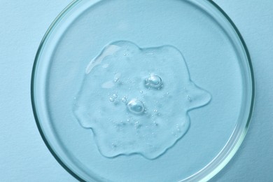 Petri dish with sample of cosmetic oil on light blue background, top view