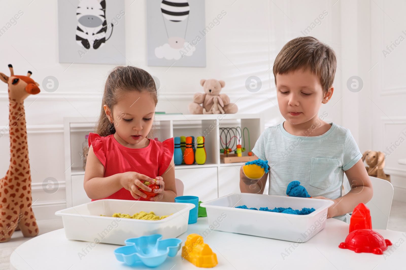 Photo of Cute little children playing with bright kinetic sand at table in room