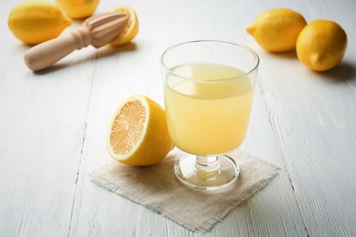 Glass with fresh lemon juice and fruit on table