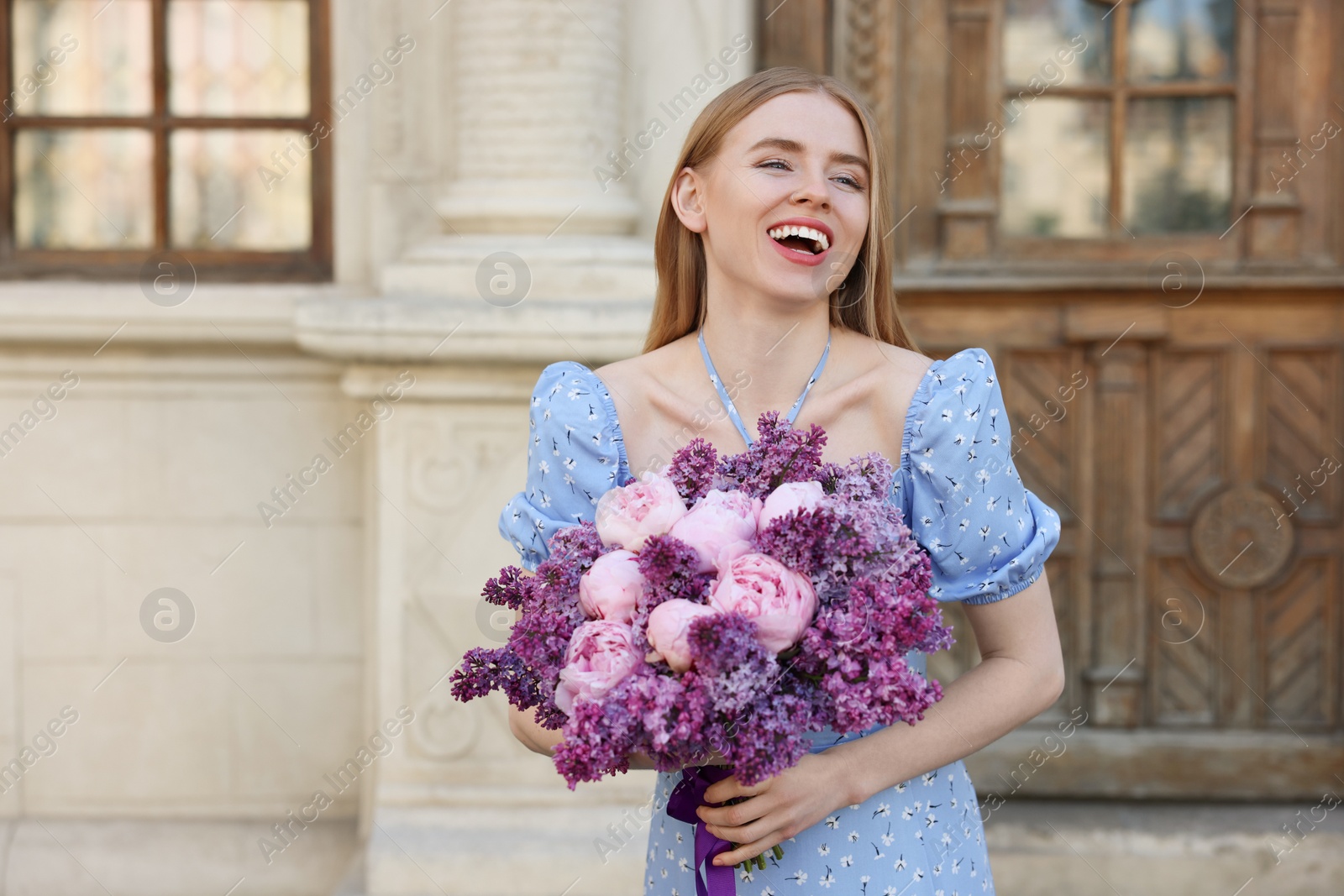 Photo of Beautiful woman with bouquet of spring flowers near building outdoors, space for text