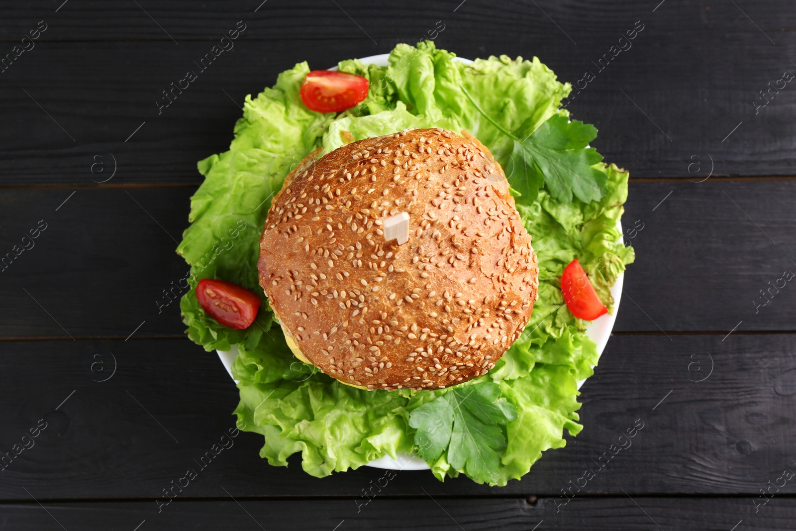 Photo of Tasty vegetarian burger on black wooden table, top view