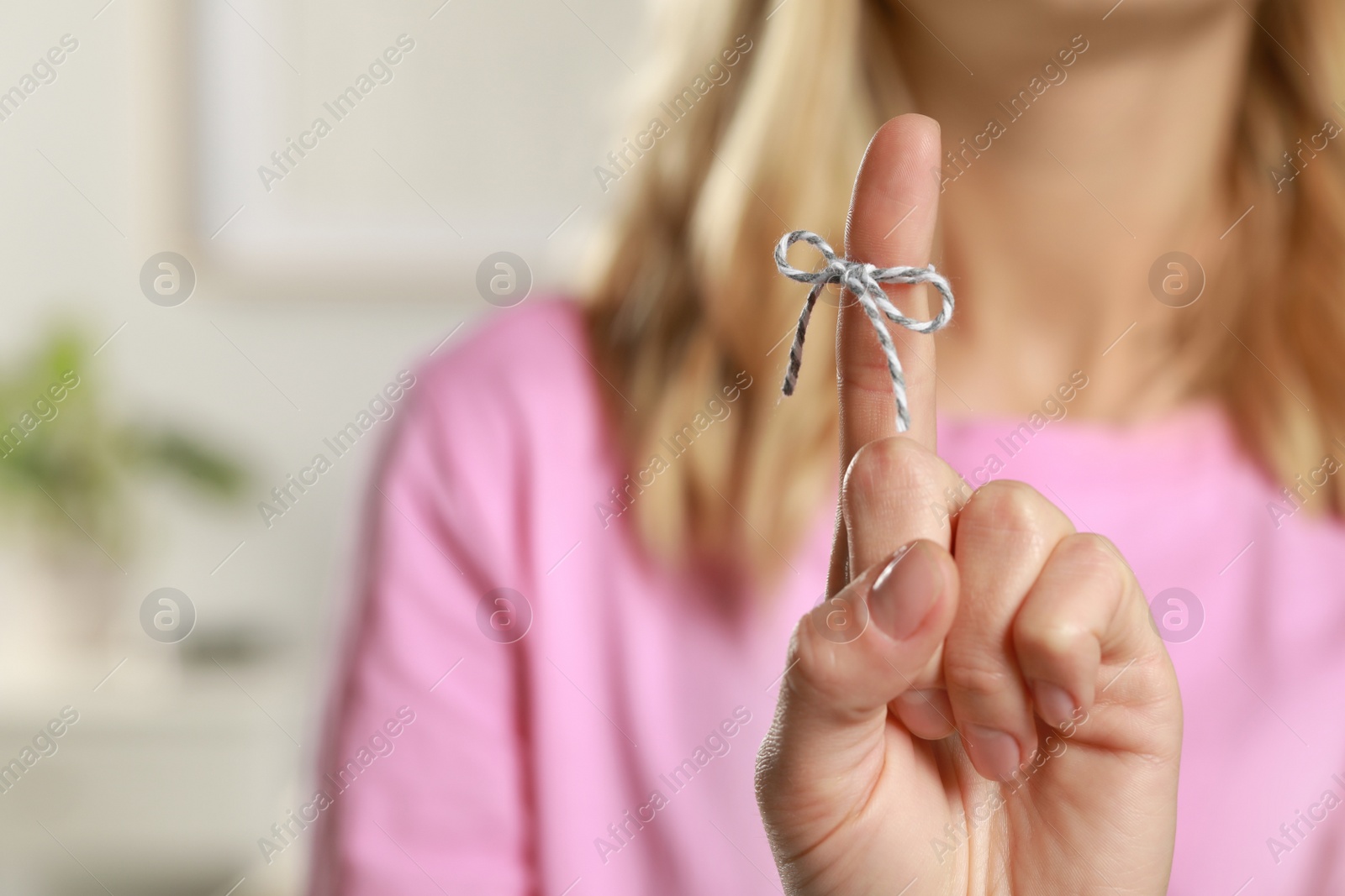Photo of Woman showing index finger with tied bow as reminder against blurred background, focus on hand