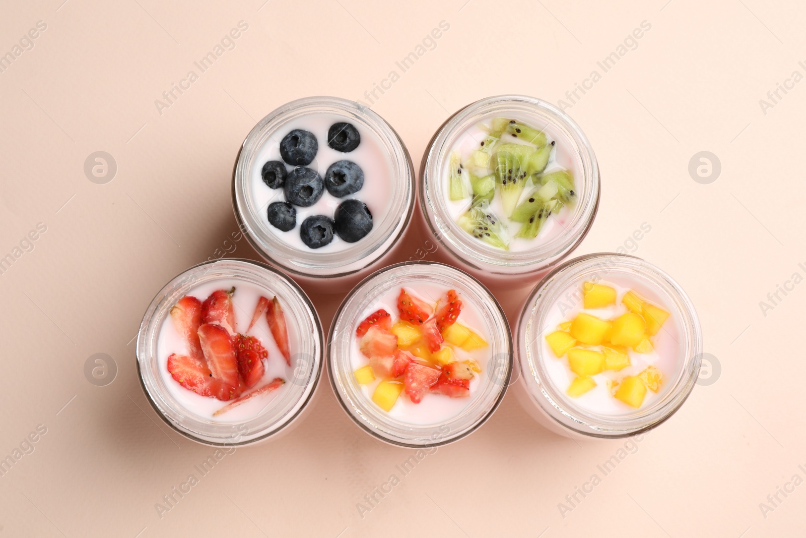 Photo of Jars of fresh yogurt and different fruits on light pink background, flat lay