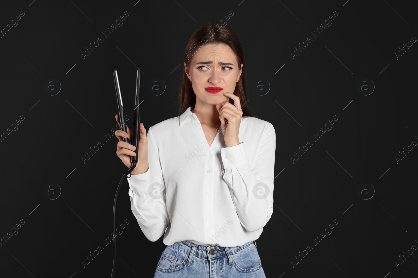 Photo of Upset young woman with flattening iron on black background. Hair damage