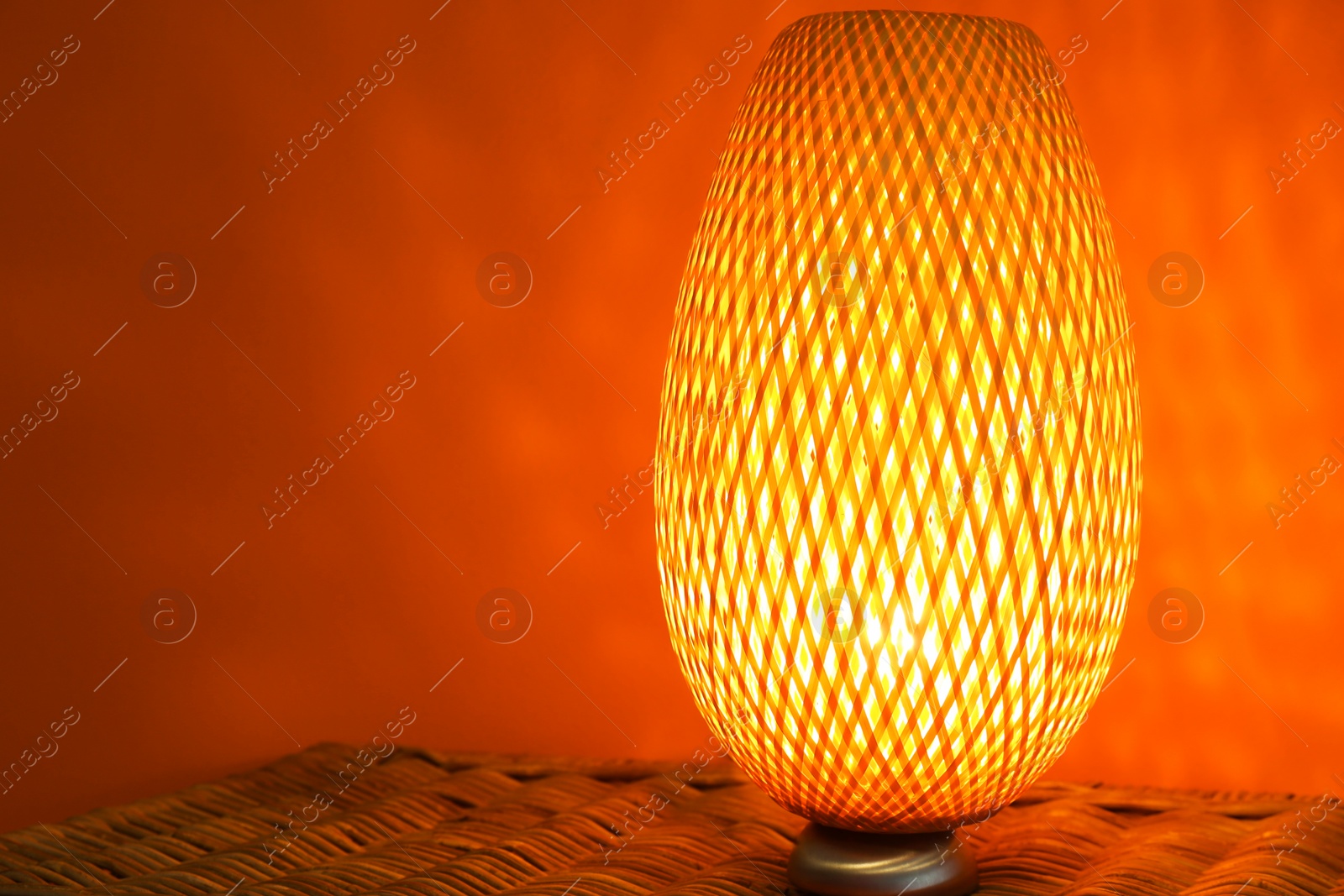 Photo of Modern lamp on wicker chest against color background. Space for text