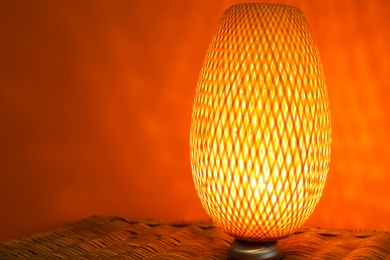 Photo of Modern lamp on wicker chest against color background. Space for text