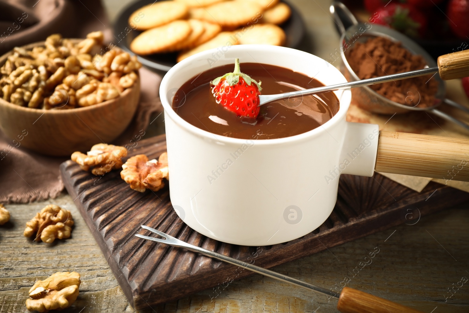 Photo of Dipping strawberry into fondue pot with milk chocolate on wooden table