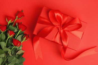 Photo of Beautiful gift box with bow and roses on red background, flat lay