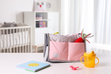 Photo of Maternity bag with baby accessories on table indoors. Space for text