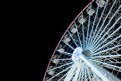 Beautiful glowing Ferris wheel against dark sky, low angle view. Space for text