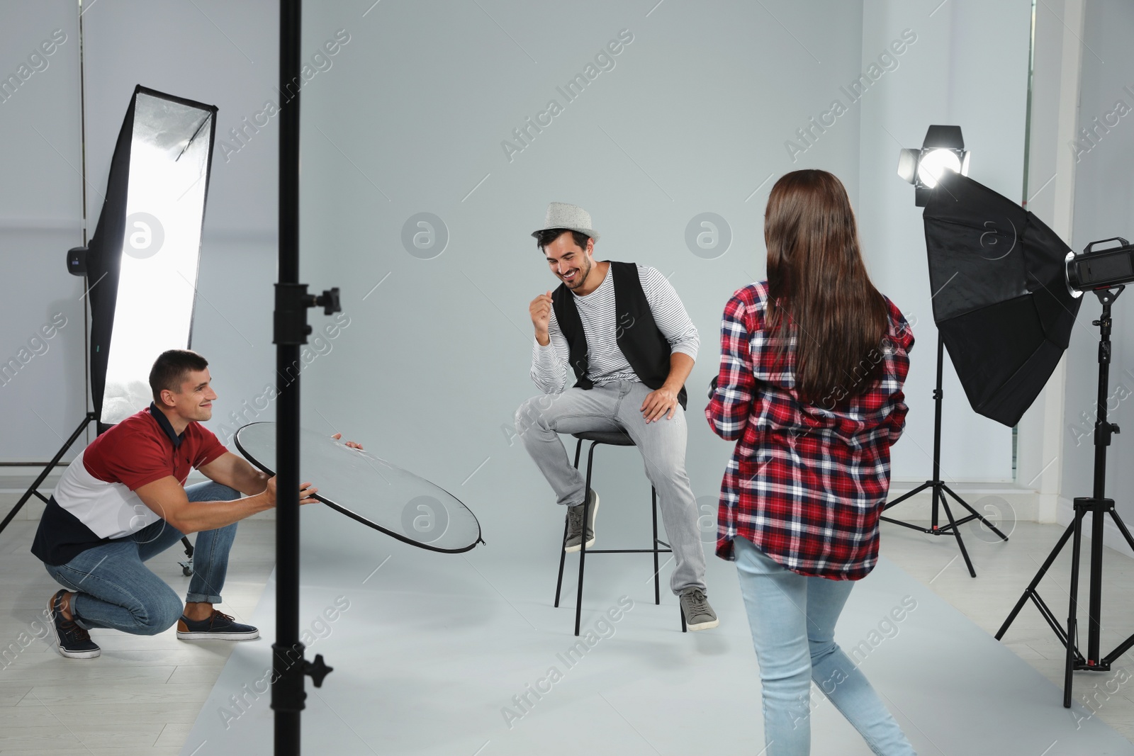 Photo of Professional photographer with assistant taking picture of young man in modern studio