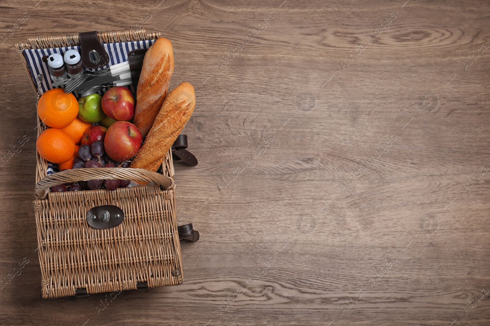 Photo of Wicker picnic basket with different products on wooden table, top view. space for text