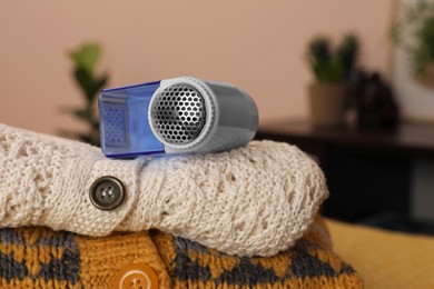 Modern fabric shaver and knitted clothes on orange blanket indoors, closeup