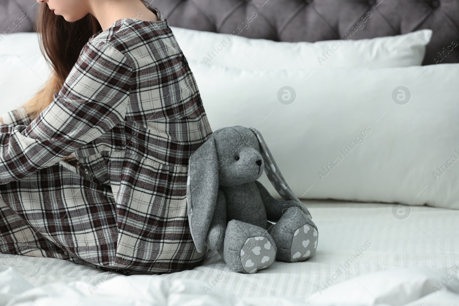 Photo of Upset teenage girl with toy sitting on bed. Space for text