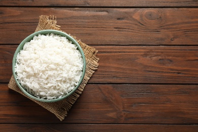 Photo of Bowl of tasty cooked rice on wooden background, top view. Space for text
