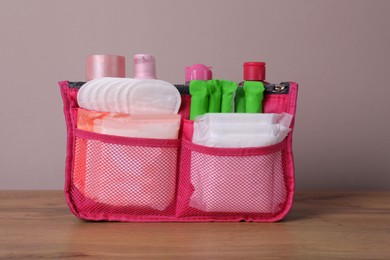 Photo of Organizer bag with menstrual pads, tampons and skin care products on wooden table