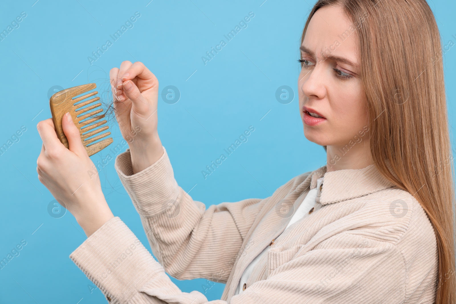 Photo of Emotional woman untangling her lost hair from comb on light blue background. Alopecia problem