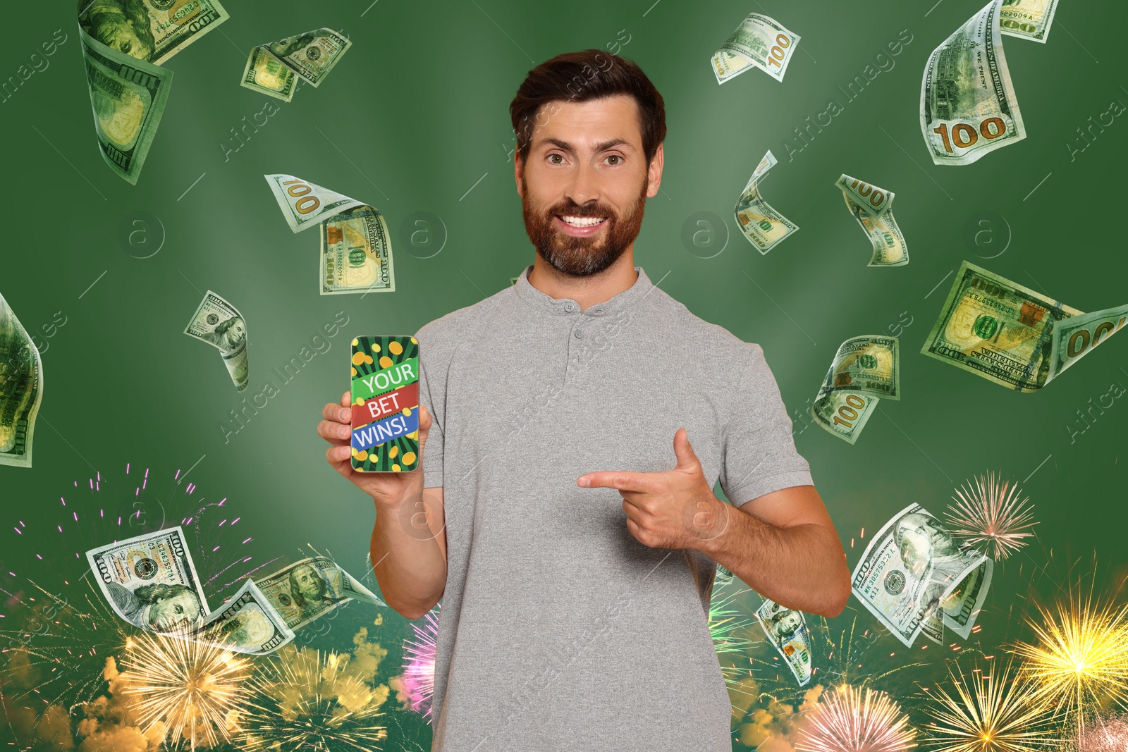 Image of Your Bet Wins! Happy man pointing at smartphone under money shower against green background with fireworks