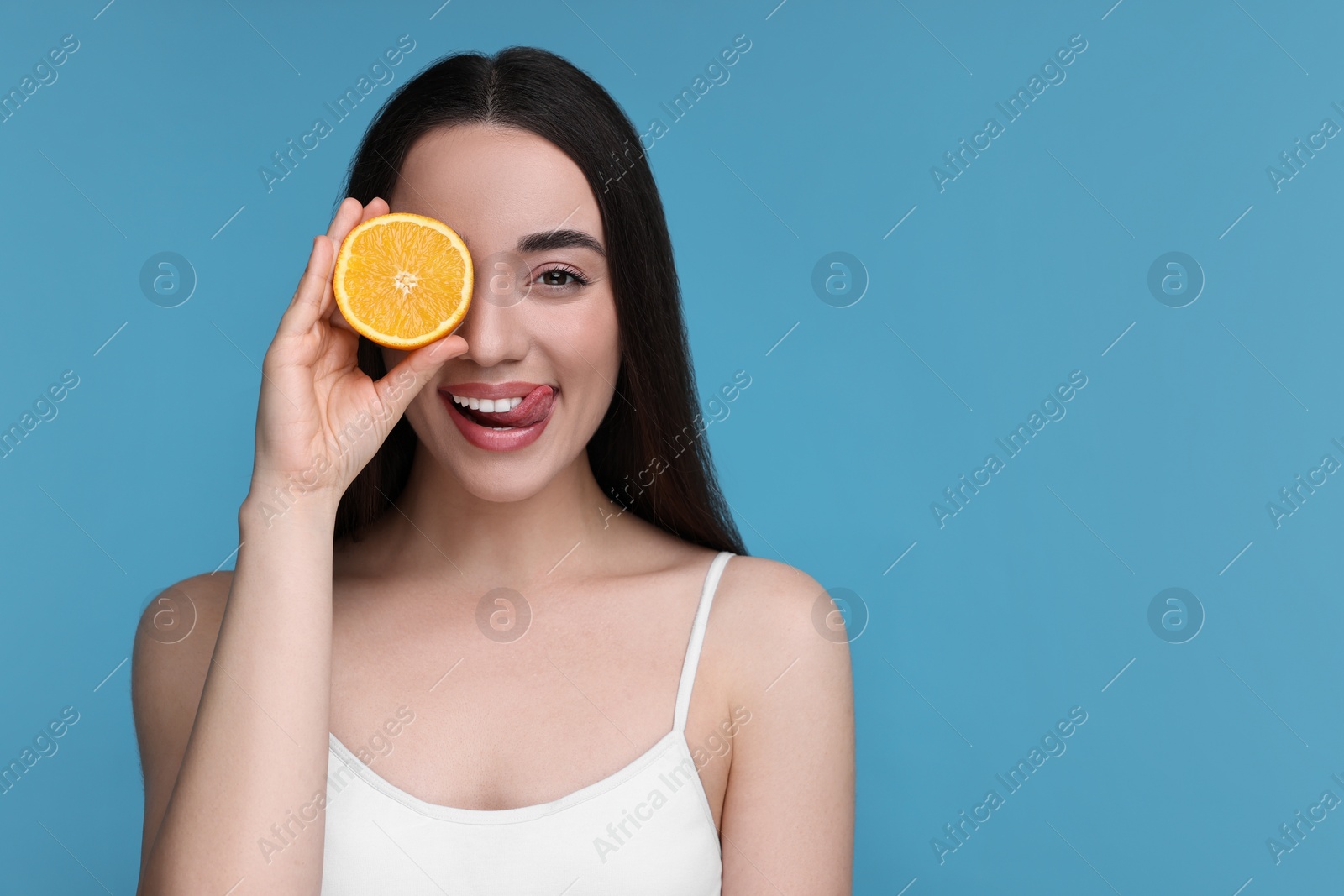 Photo of Beautiful young woman with piece of orange on light blue background. Space for text