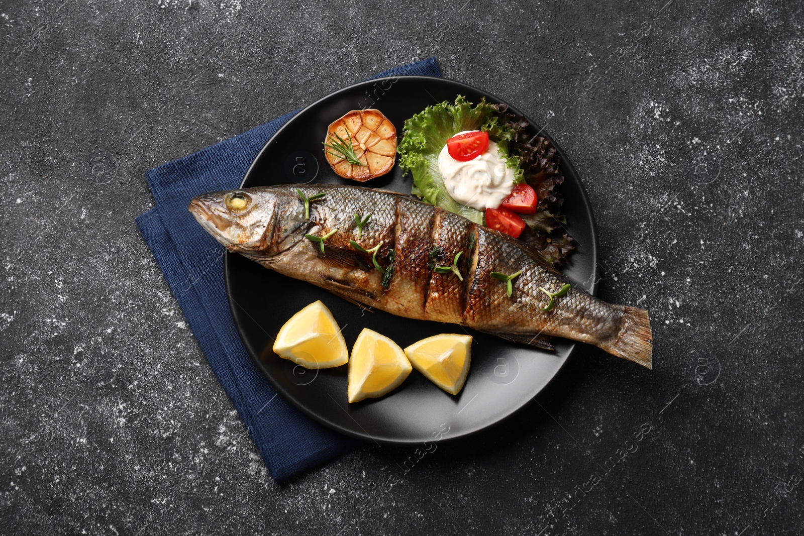 Photo of Plate with delicious sea bass fish and ingredients on dark grey table, top view
