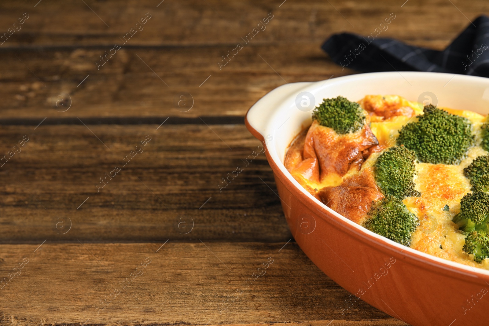 Photo of Tasty broccoli casserole in baking dish on wooden table. Space for text