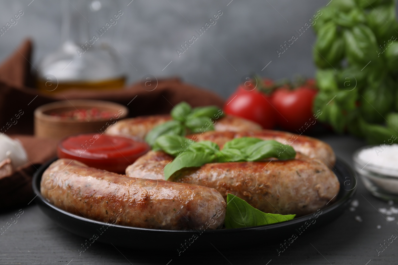 Photo of Tasty homemade sausages and basil leaves on grey wooden table, closeup