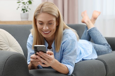 Photo of Happy woman sending message via smartphone on couch at home