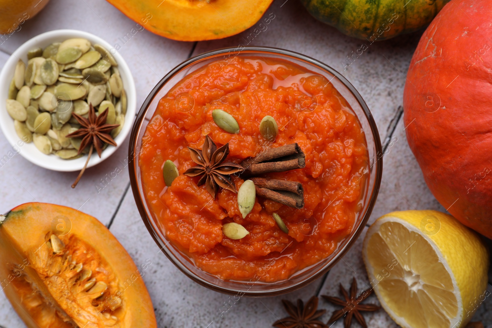 Photo of Bowl of delicious pumpkin jam and ingredients on tiled surface, flat lay