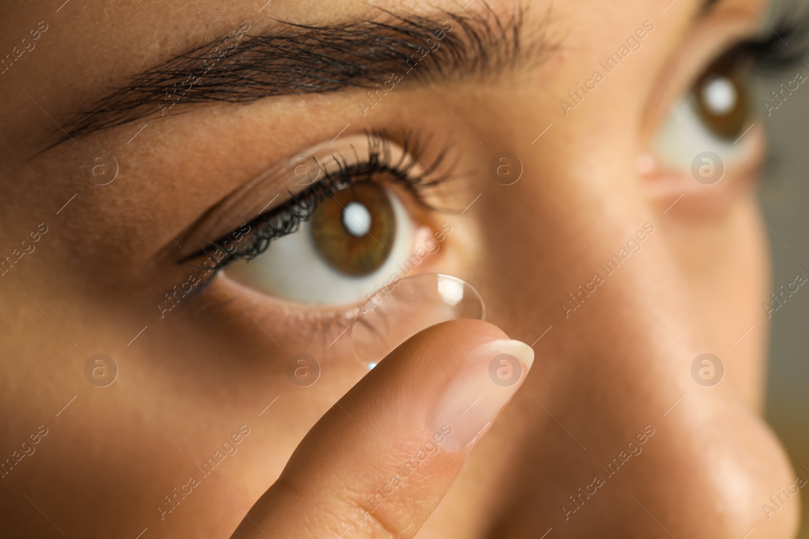 Photo of Young woman putting contact lens in her eye, closeup