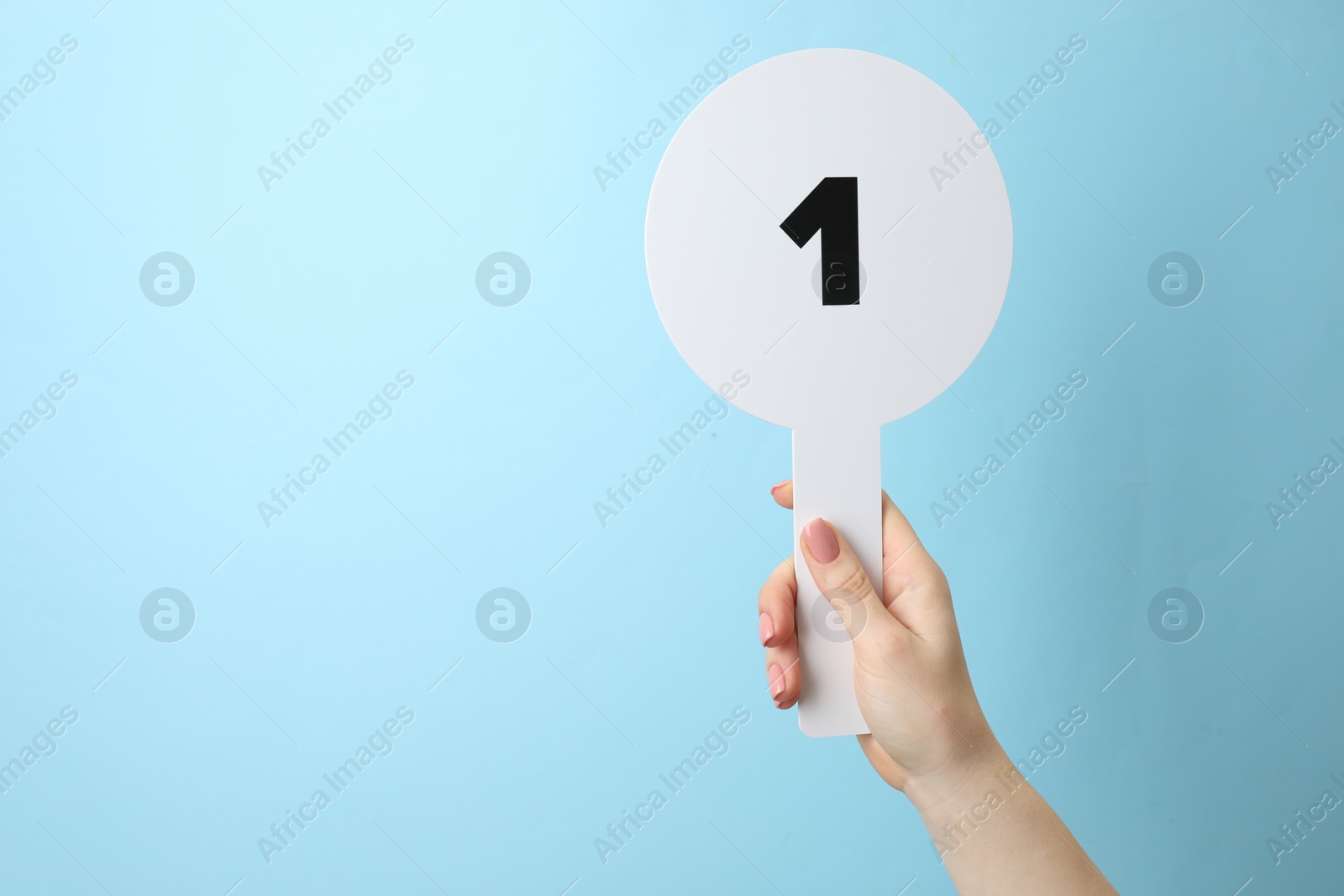 Photo of Woman holding auction paddle with number 1 on light blue background, closeup. Space for text