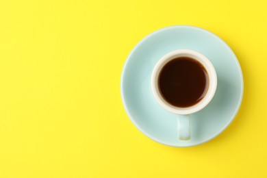 Photo of Tasty coffee in cup on yellow background, top view. Space for text