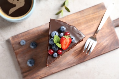 Photo of Wooden board with chocolate sponge berry cake and cup of coffee on grey background, top view