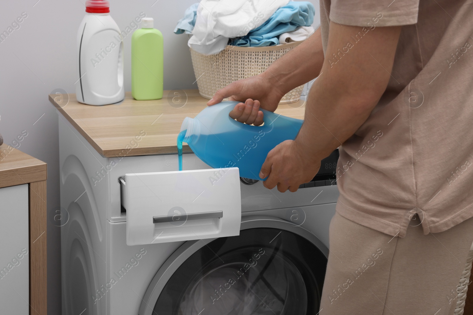 Man pouring fabric softener from bottle into washing machine indoors, closeup Photo of Man pouring fabric softener from bottle into washing machine indoors, closeup