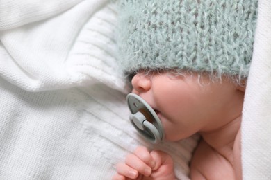 Cute newborn baby with pacifier sleeping on white blanket, top view