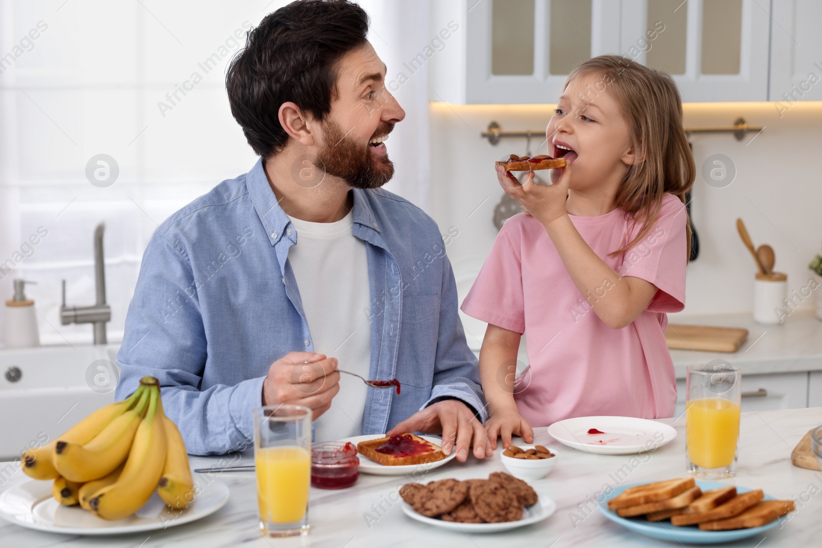 Photo of Father and his cute little daughter having breakfast at table in kitchen
