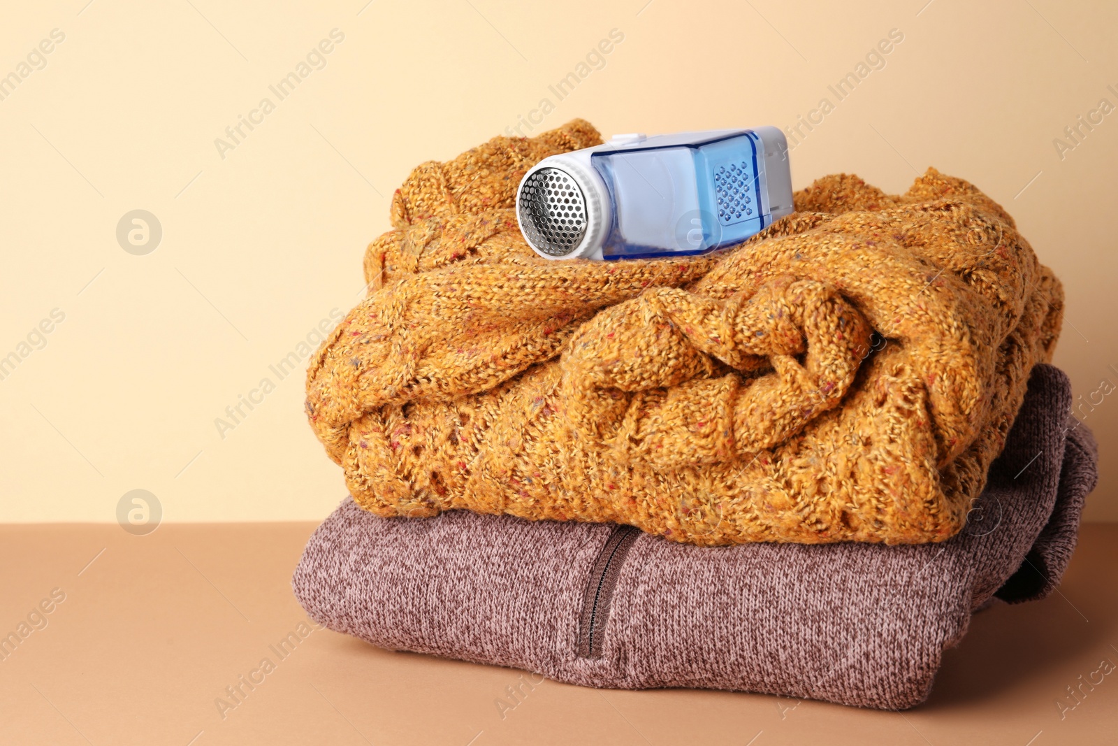 Photo of Modern fabric shaver and knitted clothes on brown table against beige wall, space for text