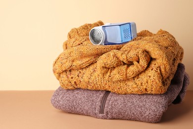 Photo of Modern fabric shaver and knitted clothes on brown table against beige wall, space for text