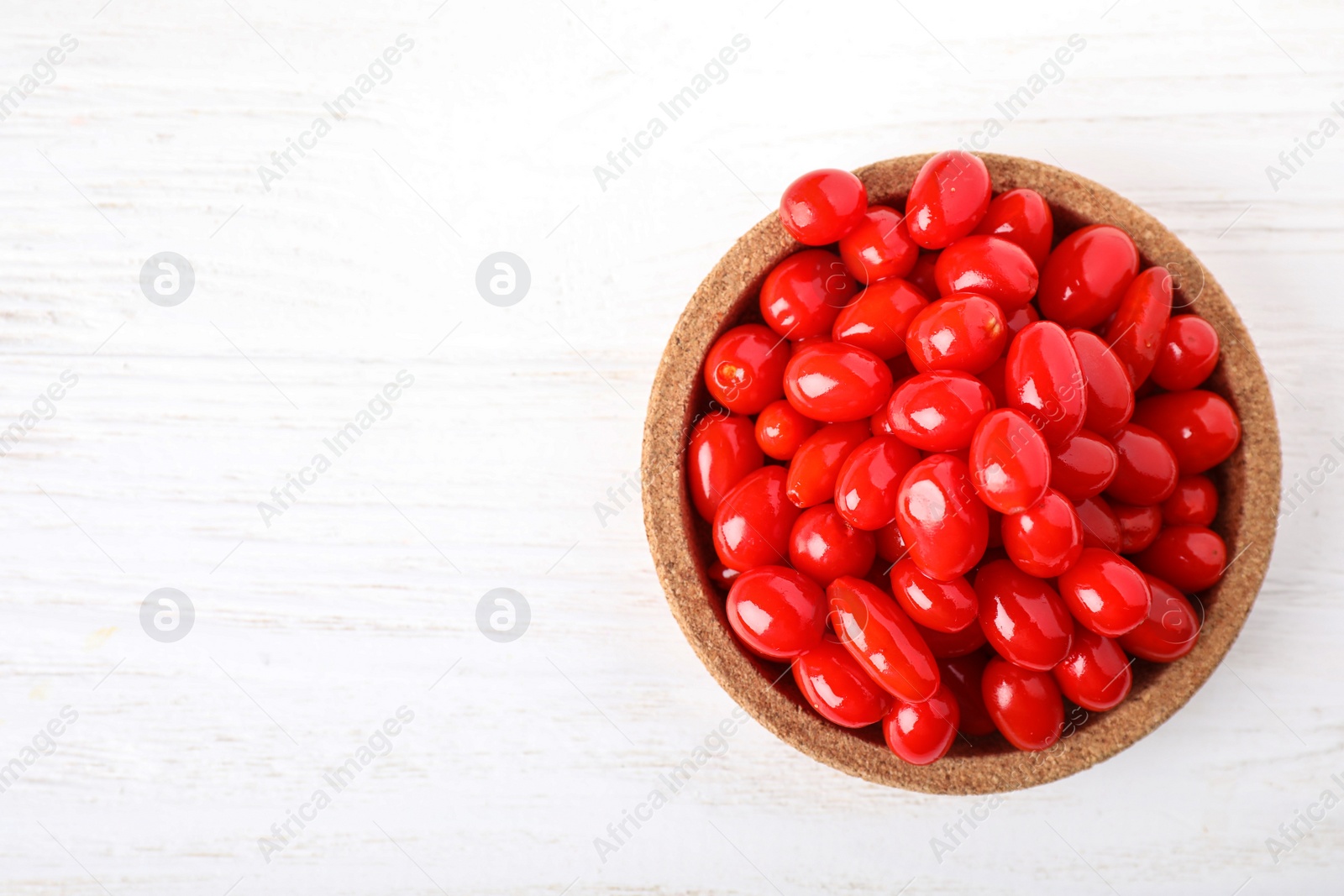 Photo of Fresh ripe goji berries in bowl on white wooden table, top view. Space for text