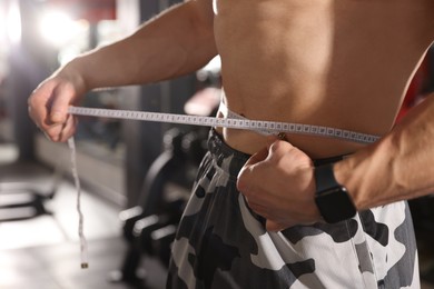 Athletic man measuring waist with tape in gym, closeup