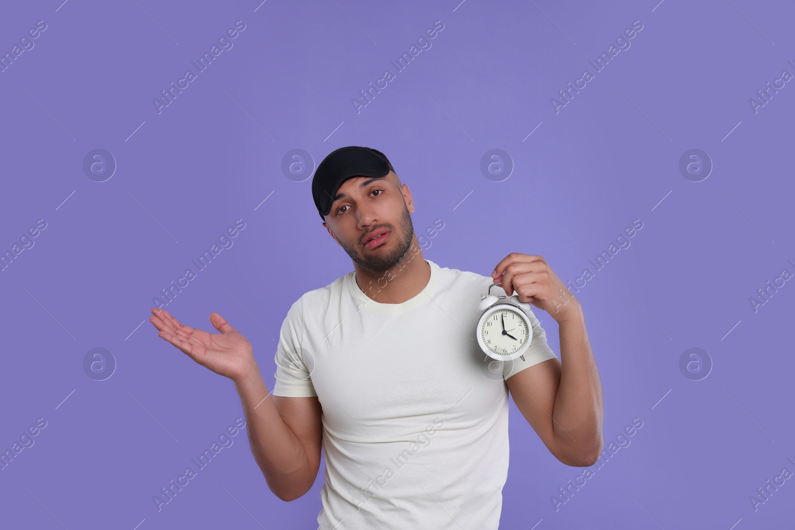 Photo of Tired man with alarm clock on violet background. Insomnia problem